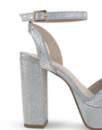 Vista trasera del tacón alto 12cm de la zapatilla plateada con plataforma, pulsera ajustable y tiras cruzadas para dama