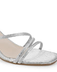 Detalle del material sintético en la zapatilla plateada de fiesta para dama con tiras cruzadas, pulsera ajustable al tobillo y tacón medio 7cm