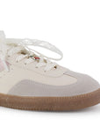 Vista de punta redonda en tenis beige con rosa para mujer con colgante en agujetas y suela baja