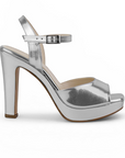 Vista lateral de zapatilla plateada para dama con plataforma, pulsera ajustable al tobillo, punta abierta y tacón alto 12cm