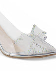 Vista a detalle de moño con pedrería en punta fina cerrada de zapatilla plateada transparente para mujer