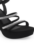 Vista a detalle de zapatilla negra para mujer con pulsera, tiras de pedrería y tacón ancho medio de 10cm