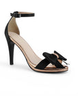 Vista diagonal de zapatilla negra de diseño descubierto para mujer con moño y pulsera al tobillo de tacón delgado de 10cm