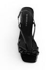 Vista superior de zapatillas negras descubiertas para mujer con moño al frente correas que suben por el empine y cierran en la parte trasera de punta cuadrada