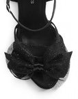 vista del detalle en el moño brilloso de zapatillas negras para dama con pulsera al tobillo y tacón alto 11cm