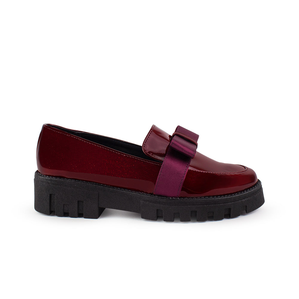Vista lateral del mocasín vino de charol para dama con plataforma chunky tipo track y moño decorativo. 