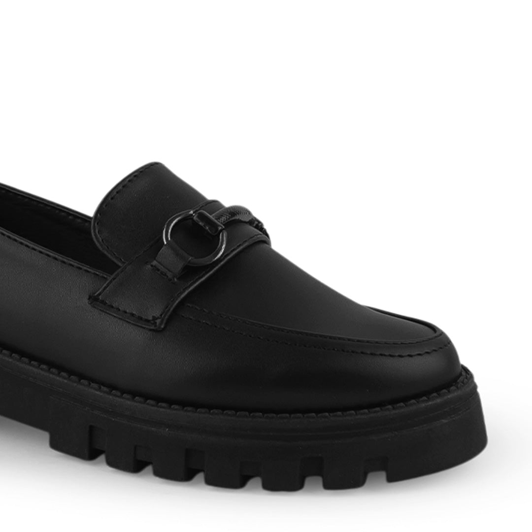 Detalle del material cabra sintético en el mocasín negro para dama con herraje decorativo y suela chunky tipo track 