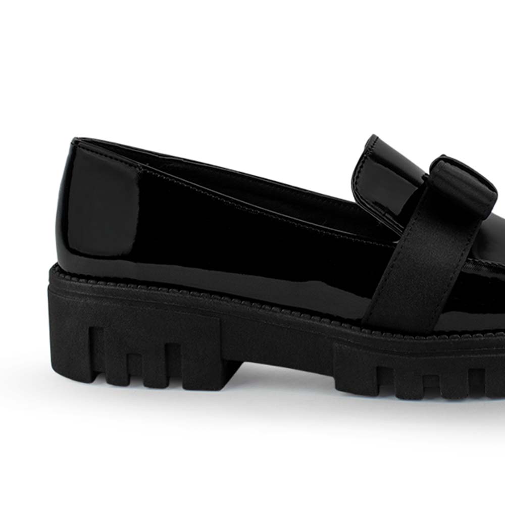 Vista trasera de la plataforma chunky o tipo track del mocasín negro en charol para dama y moño decorativo