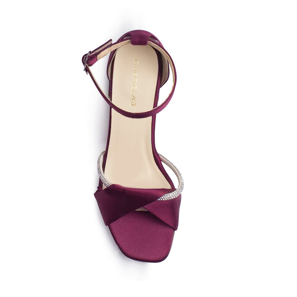 Vista superior de zapatilla para mujer con tira cruzada y banda de pedrería y pulsera ajustable al tobillo en color vino