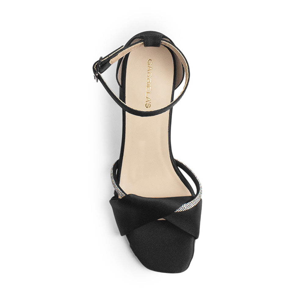Vista superior de zapatilla para mujer con tira cruzada y banda de pedrería y pulsera ajustable al tobillo en color negro