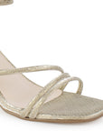 Detalle del material sintético en la zapatilla dorada de fiesta para dama con tiras cruzadas, pulsera ajustable  al tobillo y tacón medio 7cm  