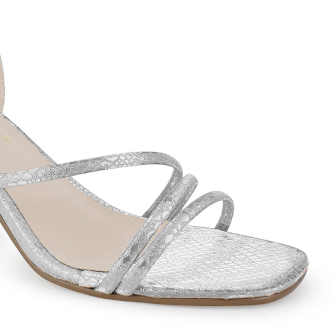 Detalle del material sintético en la zapatilla plateada de fiesta para dama con tiras cruzadas, pulsera ajustable  al tobillo y tacón medio 7cm  