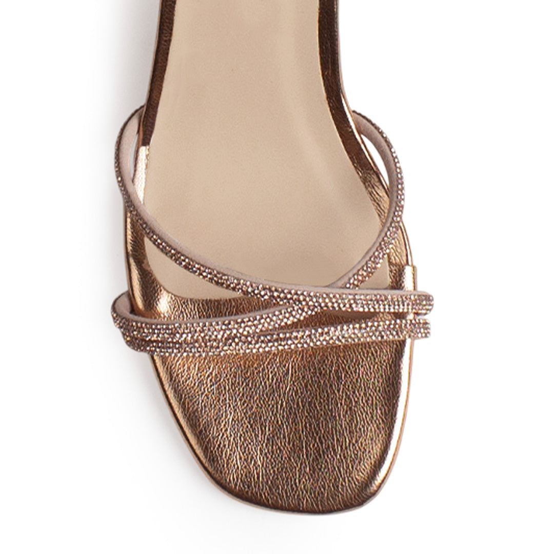 Vista de material sintético en zapatilla de diseño descubierto para mujer con tiras cruzadas con pedrería pulsera al tobillo ajustable y tacón bajo de 6cm en color oro rosa