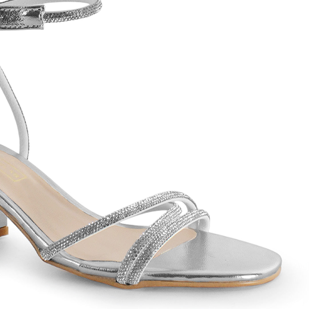 Vista a detalle de diseño descubierto con tiras de pedrería en zapatilla plateada para mujer con tacón bajo de 6cm