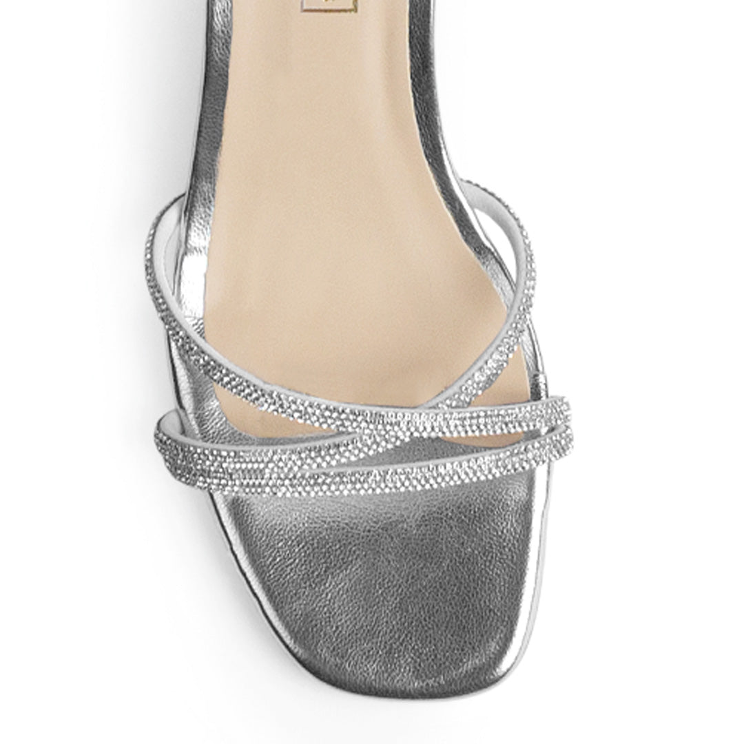 Vista de material sintético en zapatilla de diseño descubierto para mujer con tiras cruzadas con pedrería pulsera al tobillo ajustable y tacón bajo de 6cm en color plateado