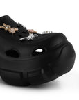 Detalle del material sintético en sandalia negra tipo clog para dama con plataforma media 7cm y charms decorativos  