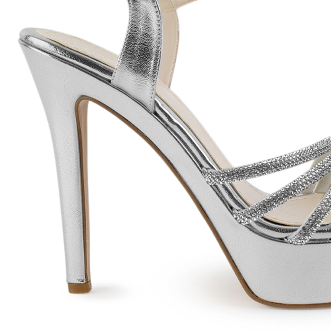 Vista trasera de tacón alto delgado de 13cm en zapatilla plateada de diseño descubierto para mujer con pedrería y pulsera ajustable al tobillo