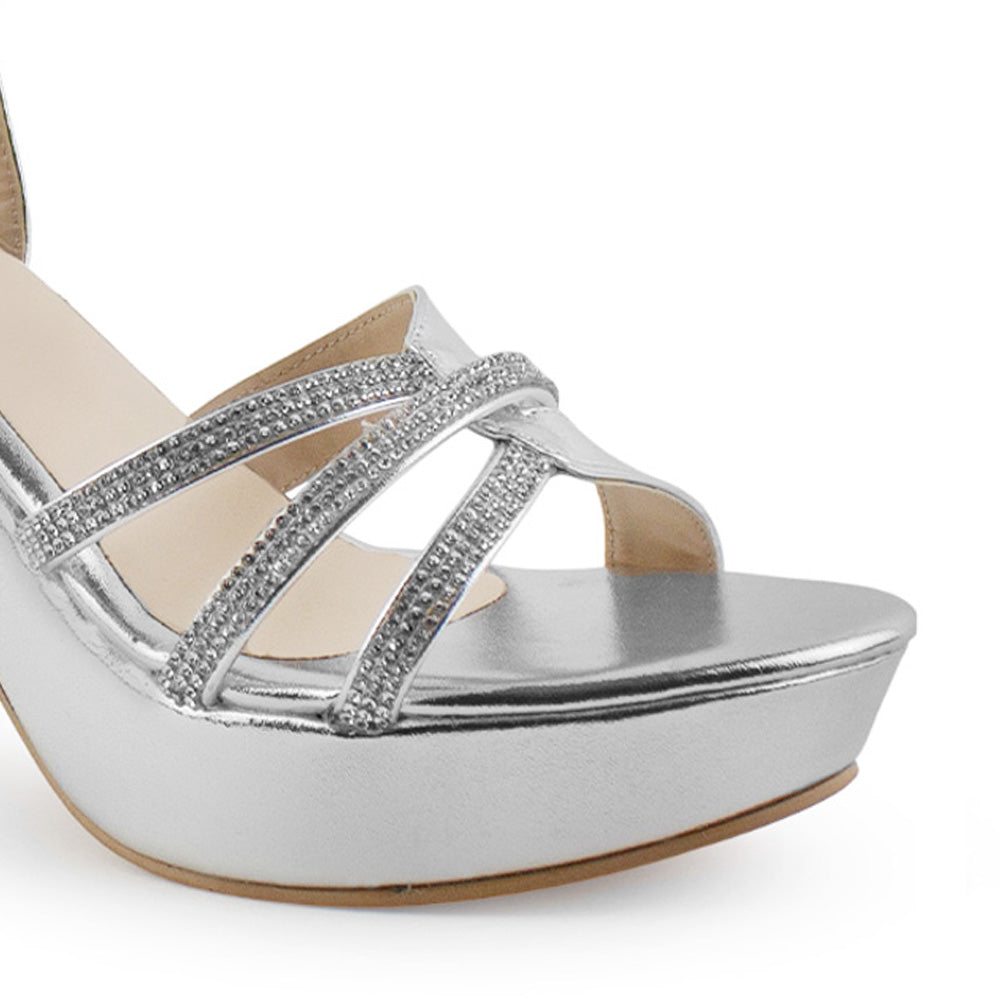 Vista a detalle de tiras cruzadas de pedrería en zapatilla plateada de plataforma para mujer con tacón de 10cm y pulsera ajustable