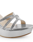 Vista a detalle de tiras cruzadas de pedrería en zapatilla plateada de plataforma para mujer con tacón de 10cm y pulsera ajustable