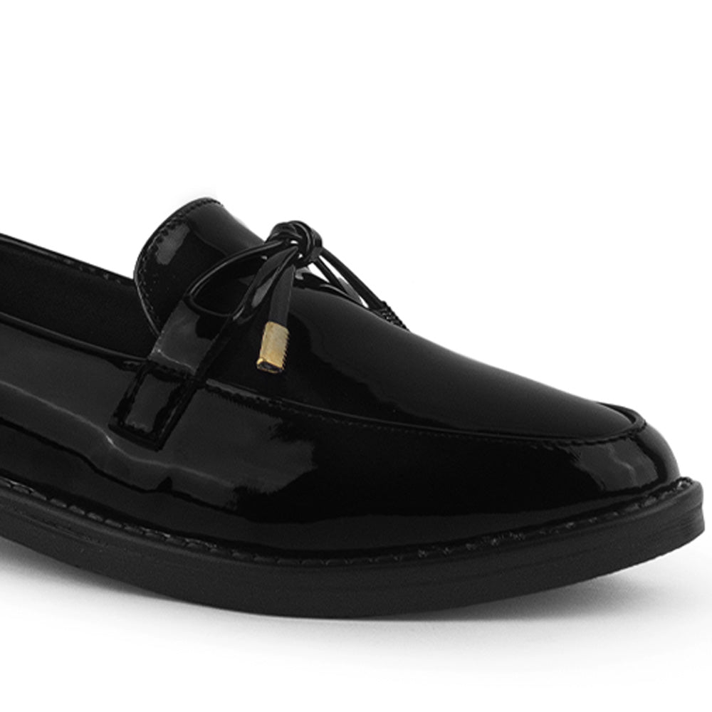 Detalle del material charol en el mocasín negro de piso para dama con moño decorativo 