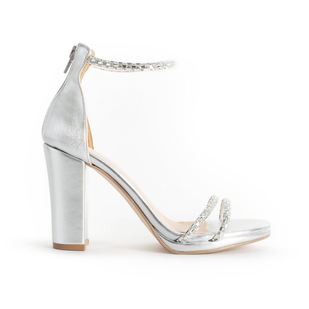 Vista lateral de zapatilla plata para mujer con tiras y pulsera de pedrería y tacón de 10cm 