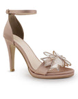 Vista diagonal de zapatilla con pulsera ajustable, moño con brillos y tacón de 10cm para mujer en color maquillaje