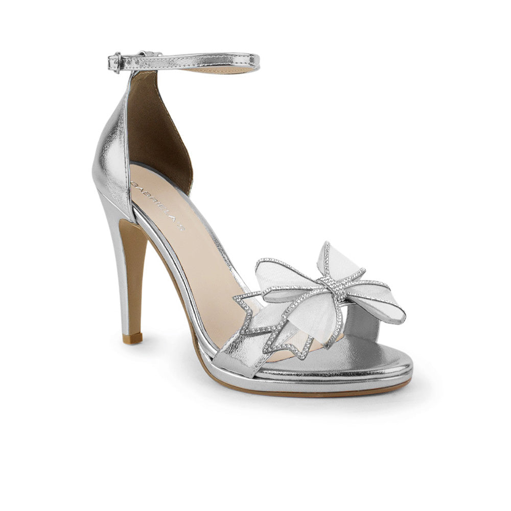 Vista diagonal de zapatilla con pulsera ajustable, moño con brillos y tacón de 10cm para mujer en color plata