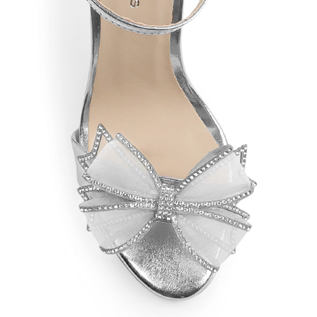 Vista de material sintético en zapatilla plata para mujer con pedreria en moño frontal y tacón delgado de 10cm