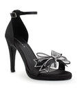 Vista diagonal de zapatilla con pulsera ajustable, moño con brillos y tacón de 10cm para mujer en color negro