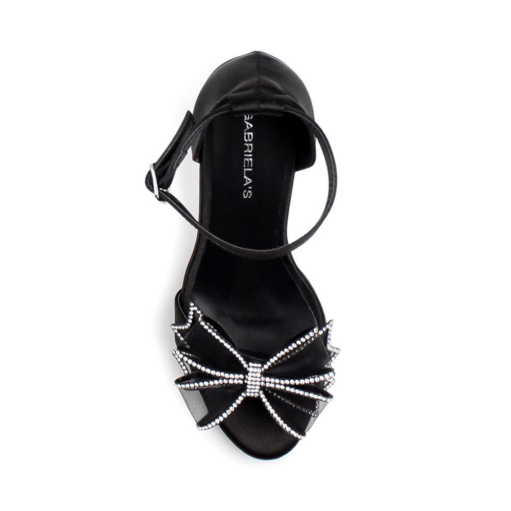 Vista superior de zapatilla negra para mujer con pulsera ajustable y moño con pedrería 