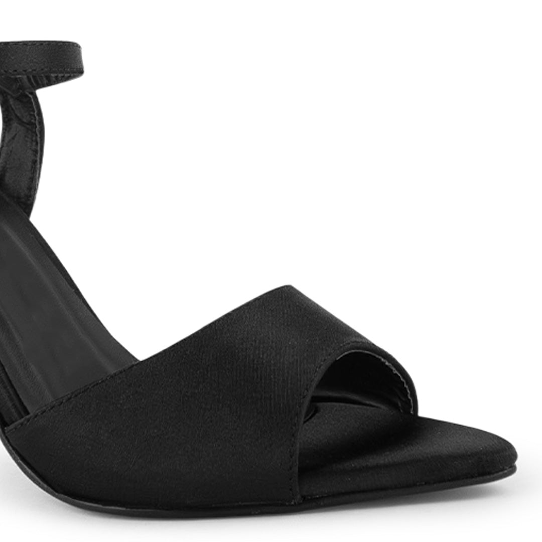 Vista a detalle de punta fina abierta en zapatilla negra para mujer con pulsera y tacón delgado de 10cm