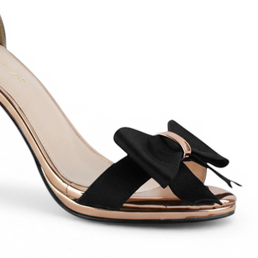 Vista a detalle de moño al frente de zapatilla negra de diseño descubierto para mujer con pulsera y tacón 10cm