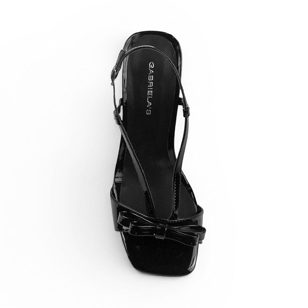 Vista superior de zapatillas negras descubiertas para mujer con moño al frente correas que suben por el empine y cierran en la parte trasera de punta cuadrada