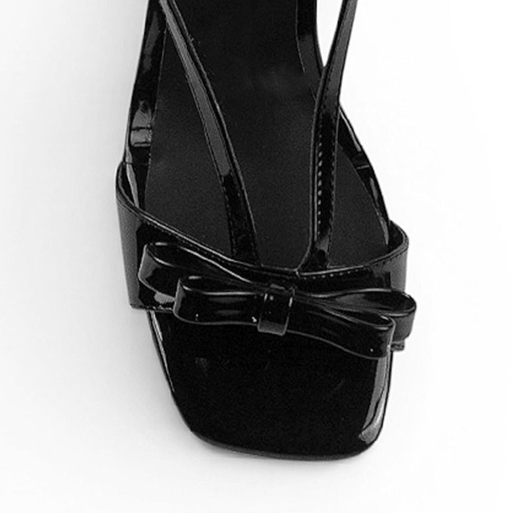 Vista de material charol en zapatilla negra de diseño descubierto para mujer con moño y tacón delgado de 8cm