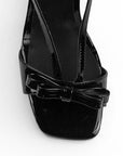 Vista de material charol en zapatilla negra de diseño descubierto para mujer con moño y tacón delgado de 8cm