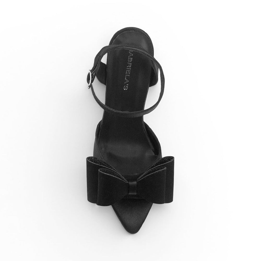 Vista superior de zapatilla negra de diseño descubierto para mujer con moño elegante punta fina y correa ajustable al tobillo 