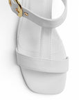 vista del detalle en tiras gruesas con hebilla dorada en zapatillas blancas de dama con tacón bajo 5cm