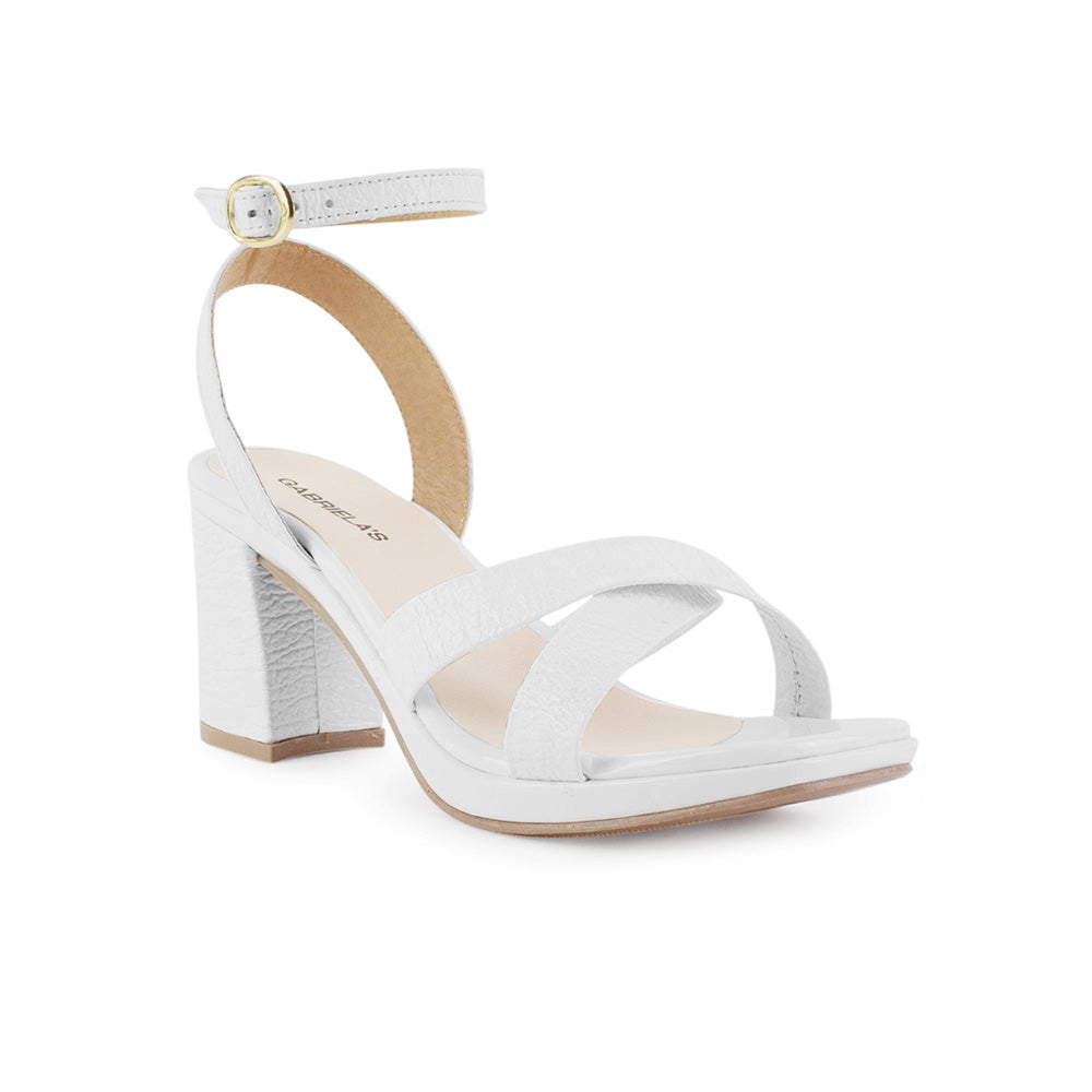 vista diagonal de las zapatillas blancas con tiras cruzadas y pulsera ajustable para dama con tacón medio 8cm