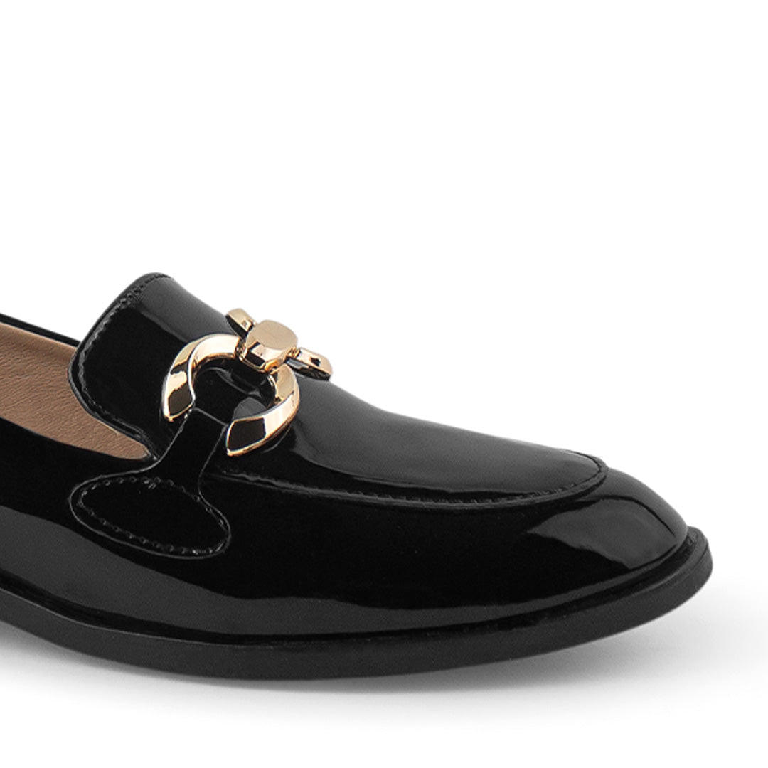 Detalle del material charol en mocasín negro con suela de piso y herraje metálico decorativo para dama 