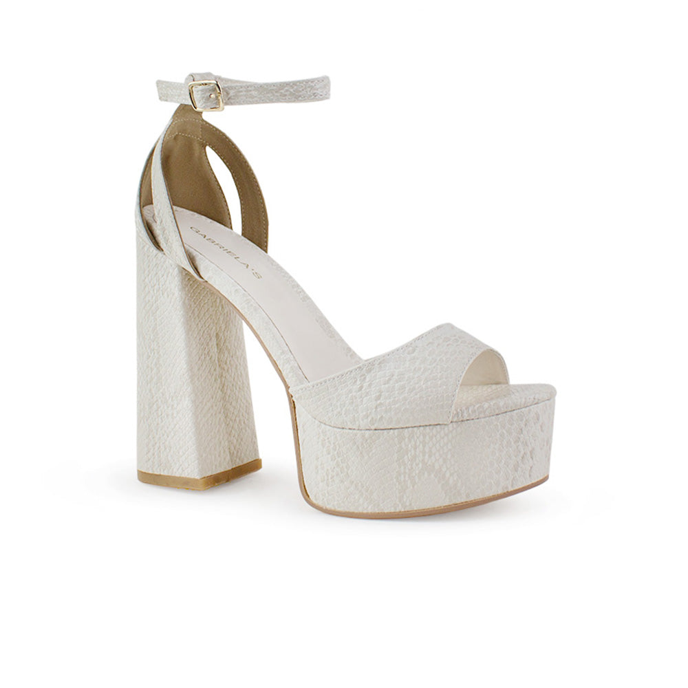 Vista diagonal de zapatilla para mujer con pulsera y tacón alto 13cm en color beige en acabado grabado